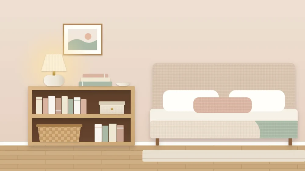 A low bookcase beside a bed with pale bedding, holding tonal books, a keepsake box and a woven basket, with a small glowing lamp, a book stack and a dish on top
