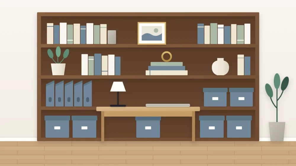 A desk with a closed laptop and lamp in front of shelving with styled books, a plant and a frame at eye level and matching boxes and magazine files below
