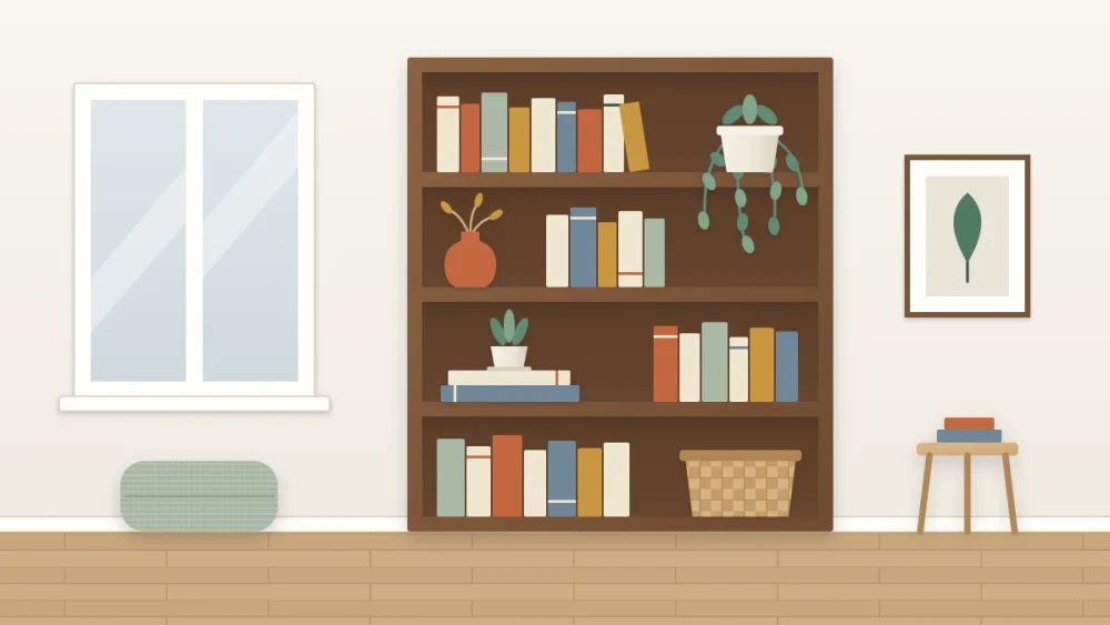 A bookcase beside a window with a trailing plant on an upper shelf, a small potted plant on a book stack and a vase of dried stems